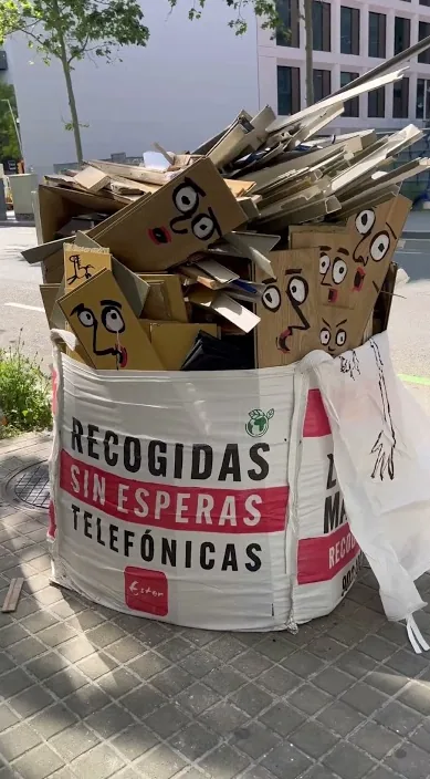 Sac de runa al carrer ple de cares pintades sobre cartró, Barcelona – Art Is Trash
