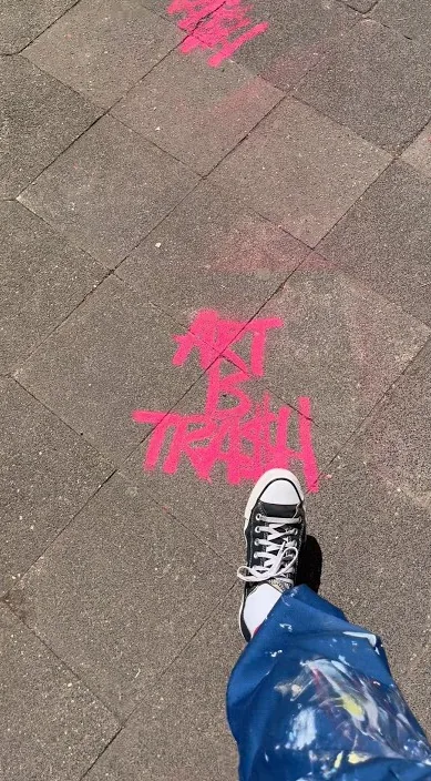 Bogstaverne Art Is Trash sprayet i pink på fortovet under en udstilling i Düsseldorf