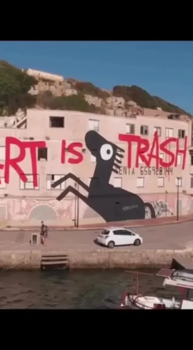 Stort vægmaleri med sort figur på en hvid væg ved vandet – Art Is Trash